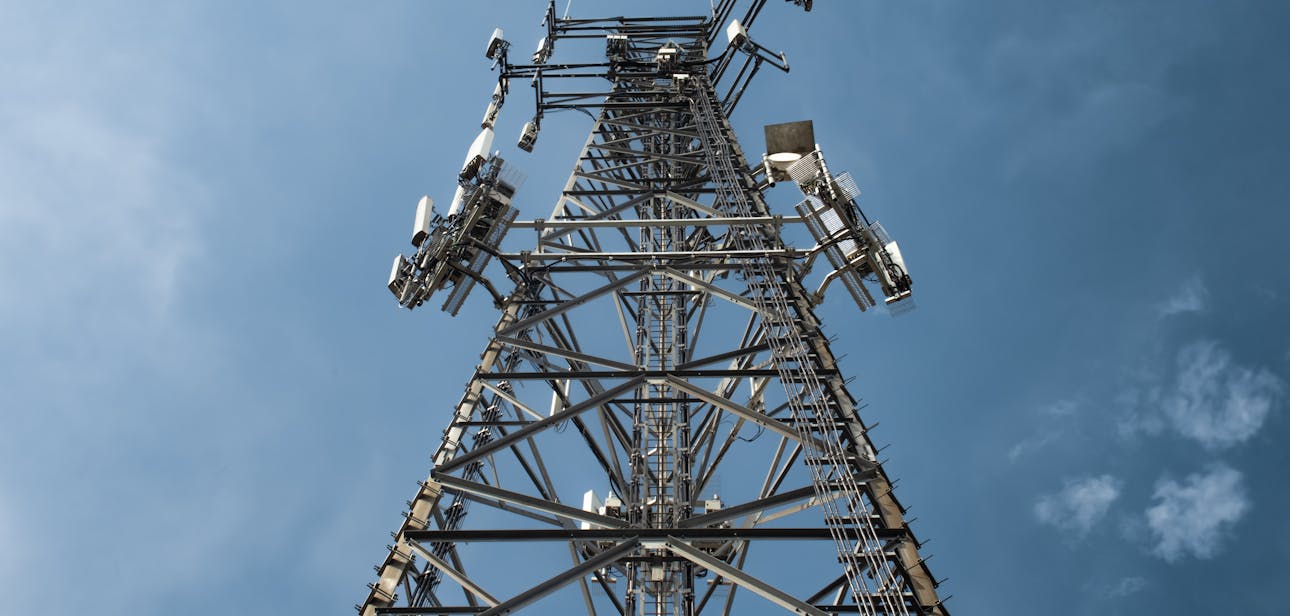 A low-angle shot of a tall metal communications tower with multiple antennas against a clear blue sky.